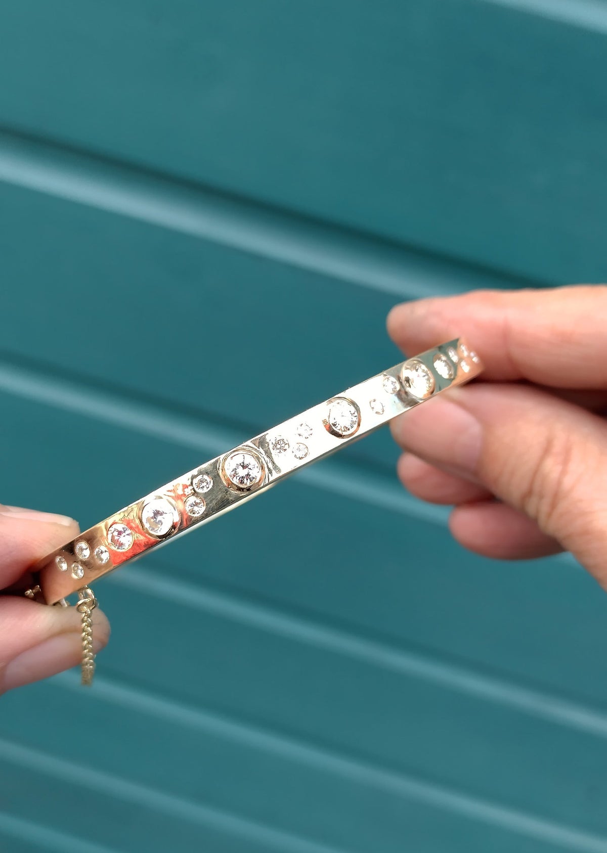 Handmade 9ct gold bangle set with round diamonds in a mix of bezel and flush settings, held in the jeweller’s hand.