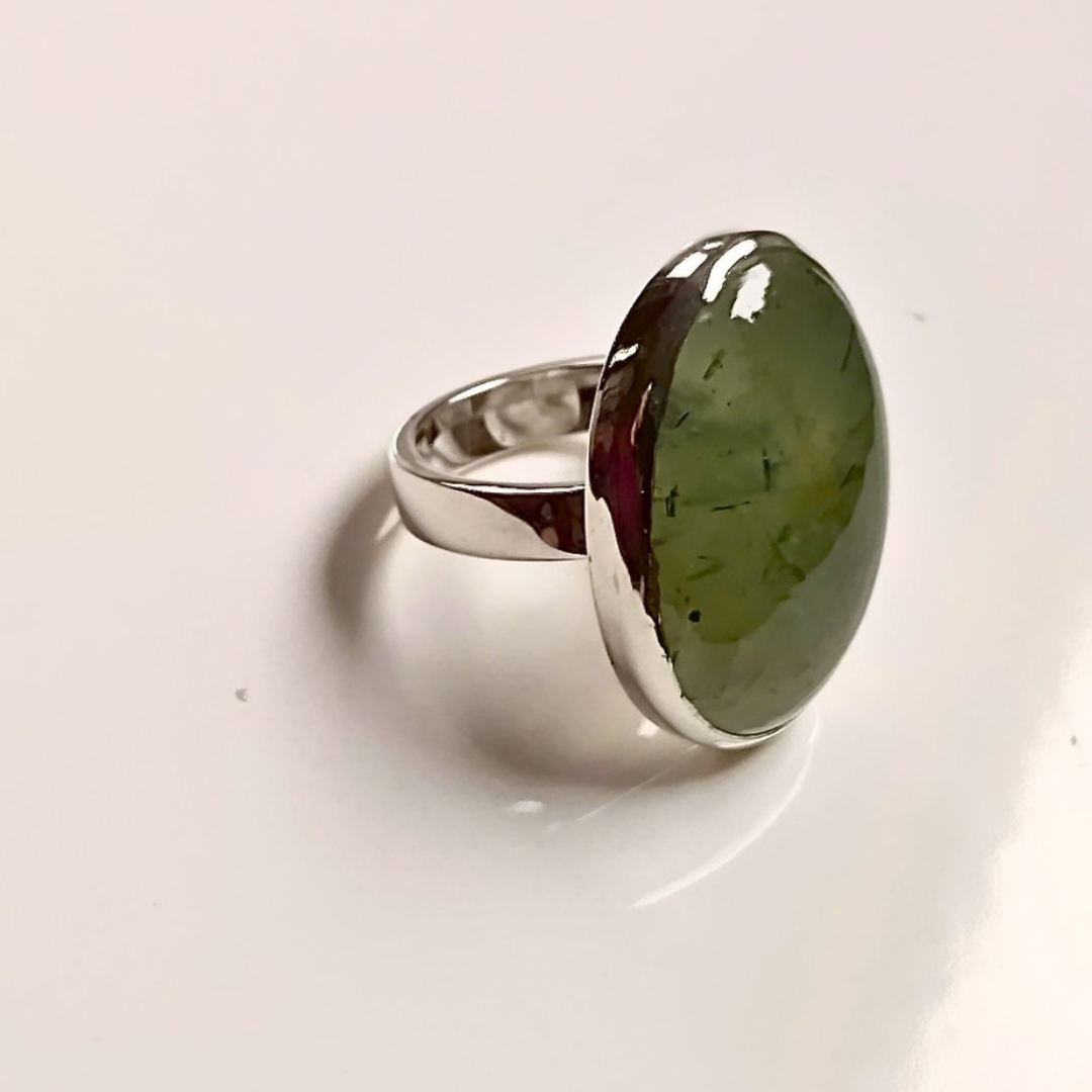 A silver ring featuring a large, oval-shaped green stone with visible inclusions, set against a plain white background.